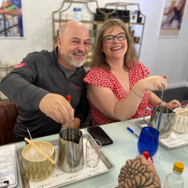 Two people stirring wax at indoor candle-making bar