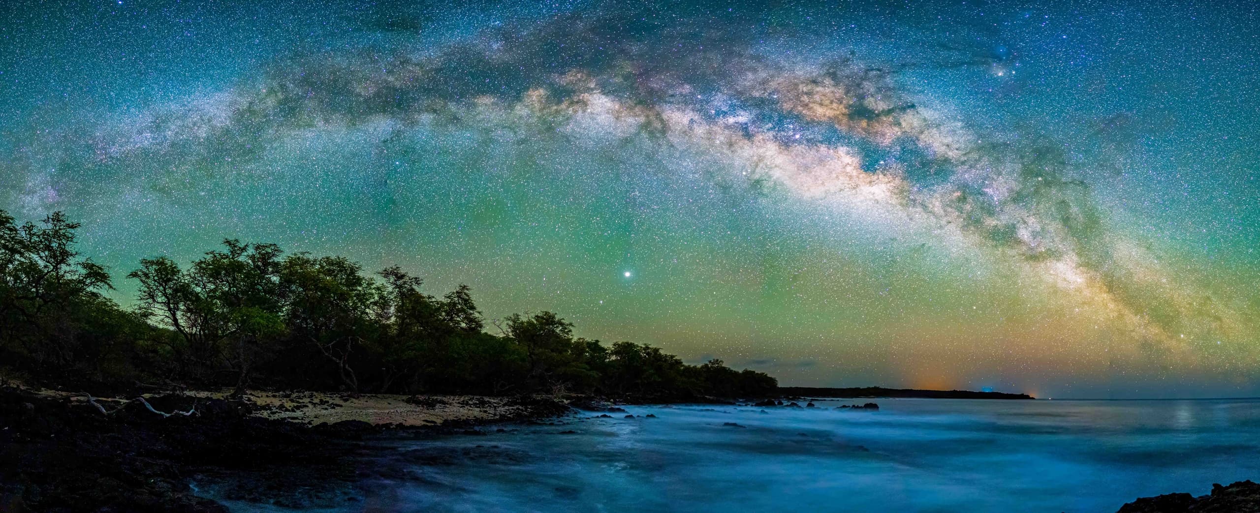 Milky Way arching over rocky shoreline at night, coastal vista