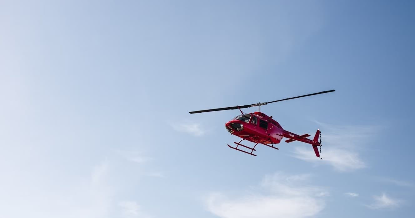 Red helicopter flying over open blue sky for scenic tour