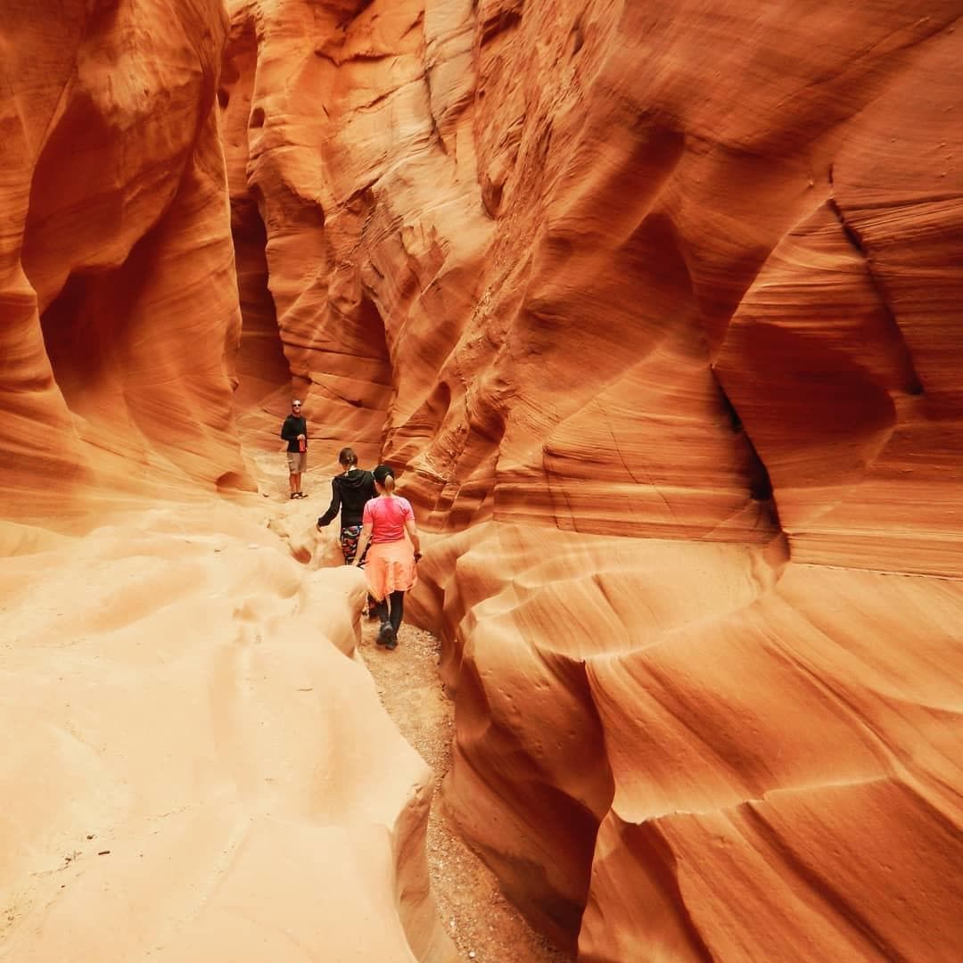 Hikers exploring narrow slot canyon with red sandstone walls