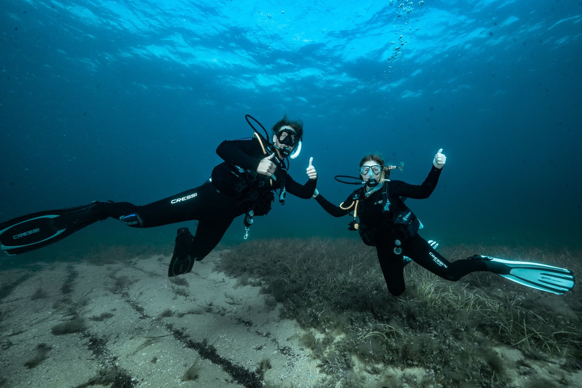 Two scuba divers waving underwater over sandy ocean floor