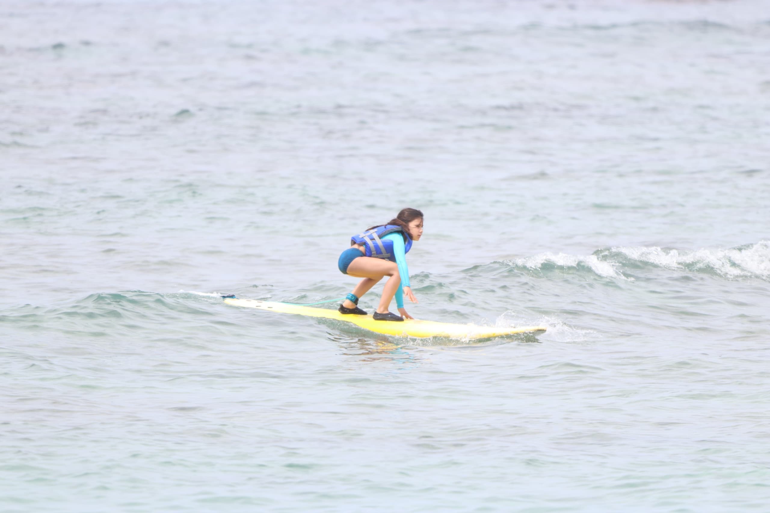 Young surfer kneeling on board in calm shallow ocean nearshore waters