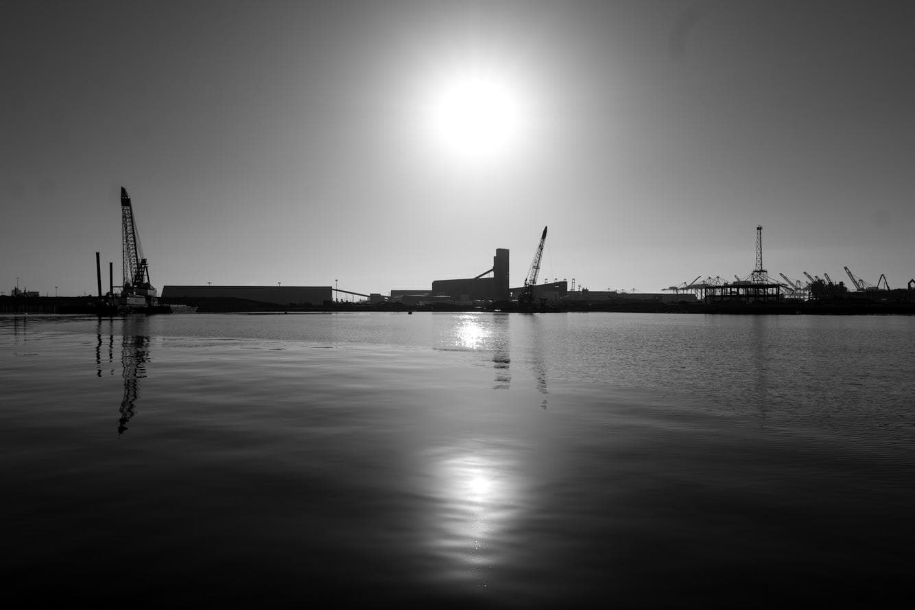 Harbor sunrise silhouette with cranes over calm water, port