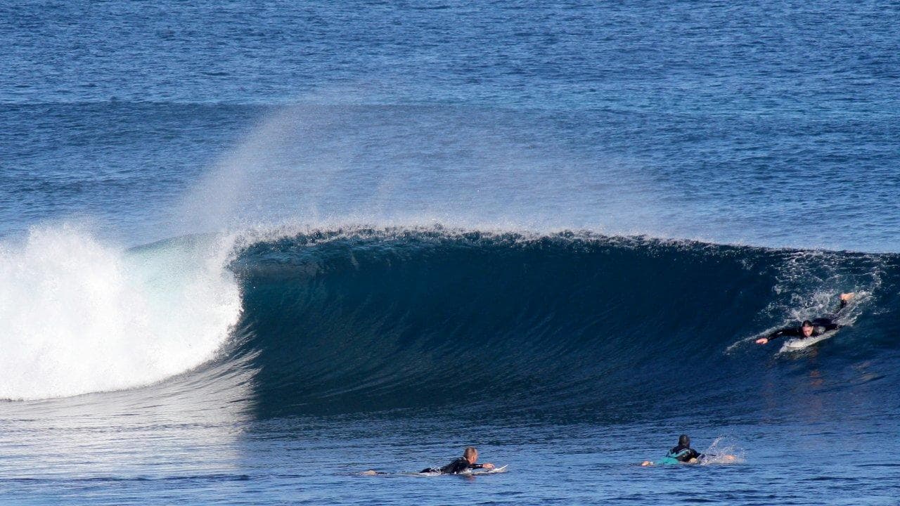 Surfers paddling and riding a barreling ocean wave at reef break