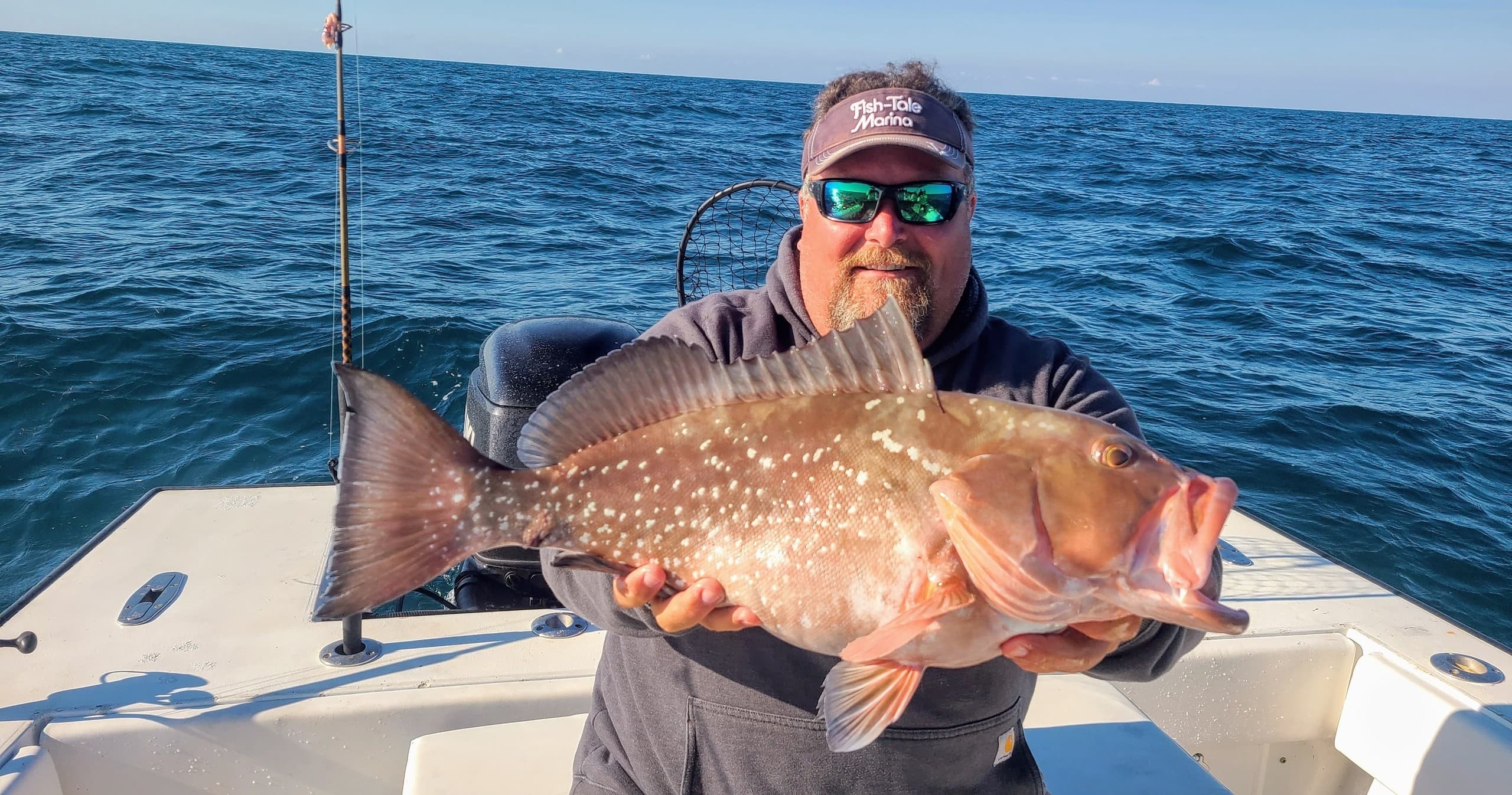 Angler holding trophy grouper on boat, offshore fishing trip