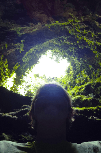 Explorer silhouetted at mossy cave skylight opening to sky