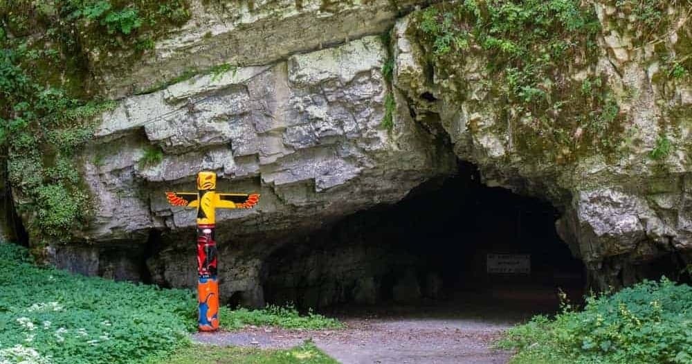 Hikers approaching a limestone cave entrance in forest