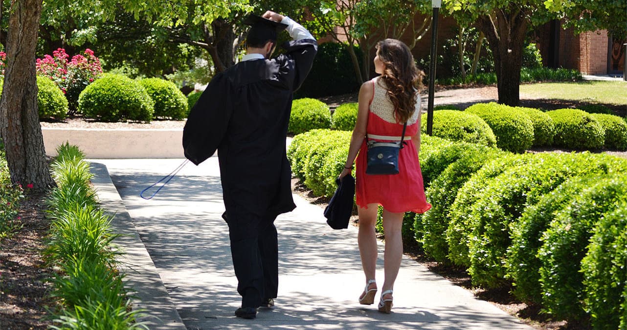 Graduates walking on tree-lined campus path, celebratory stroll