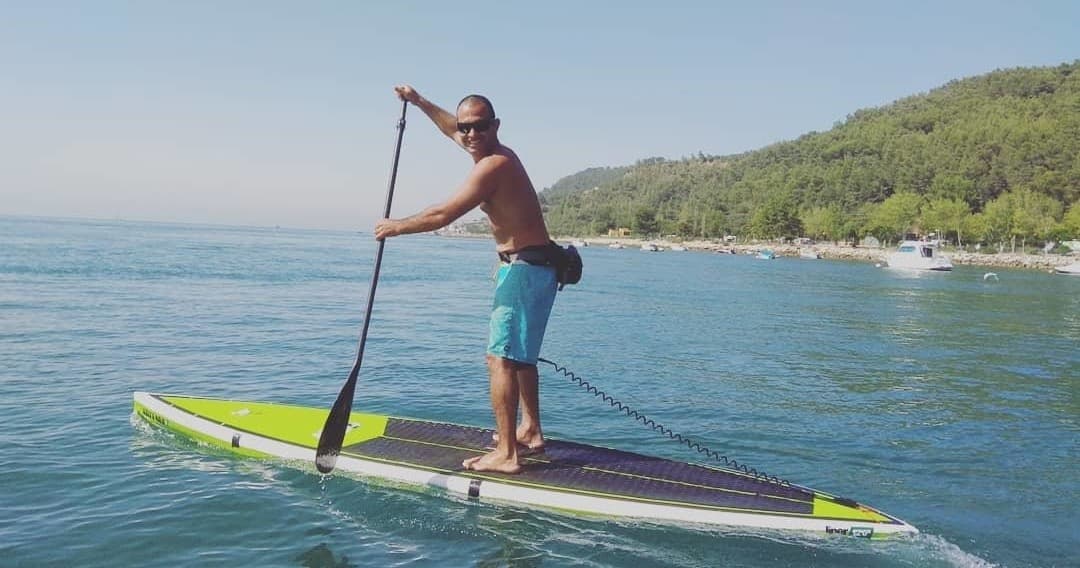 Stand-up paddleboarder paddling on clear coastal waters near forested shore