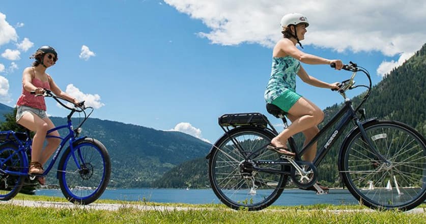 Two cyclists riding along lakeside trail with mountain views