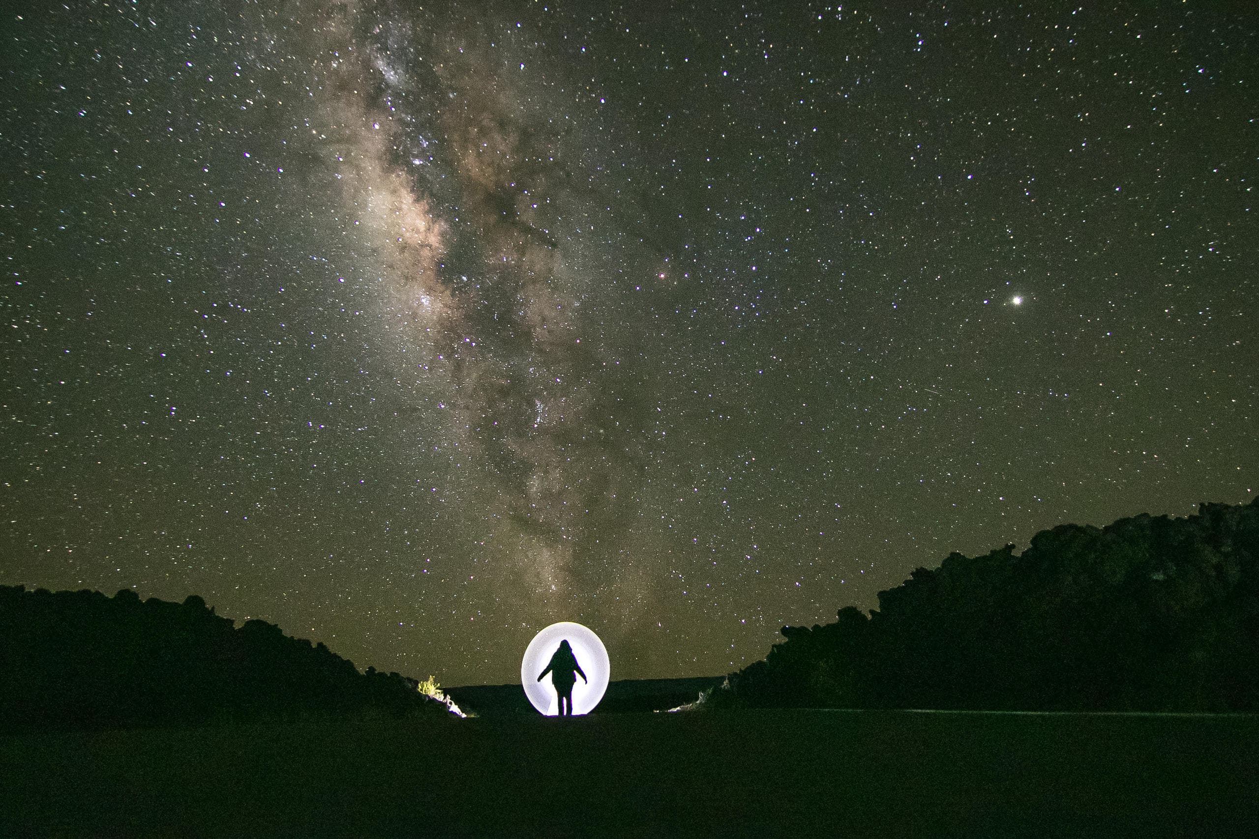 Milky Way over silhouetted explorer in dark desert landscape