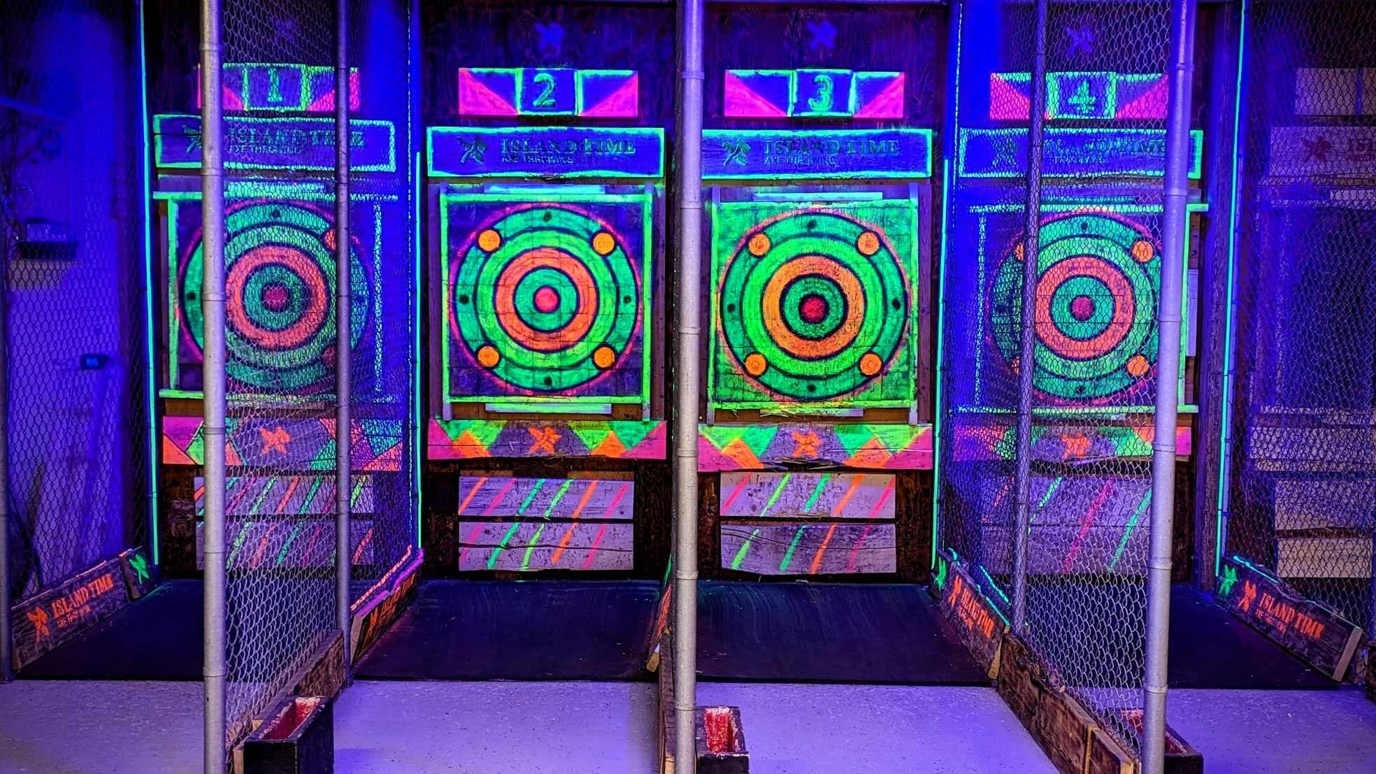 Neon axe-throwing lanes inside blacklight venue with colorful targets