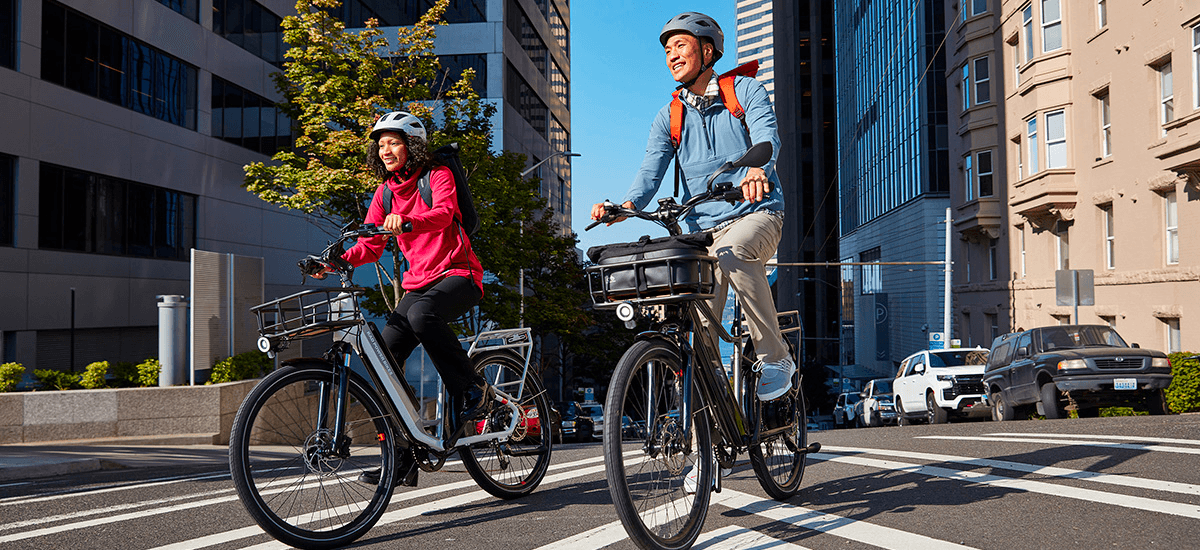 Two cyclists on e-bikes riding through city street urban commute