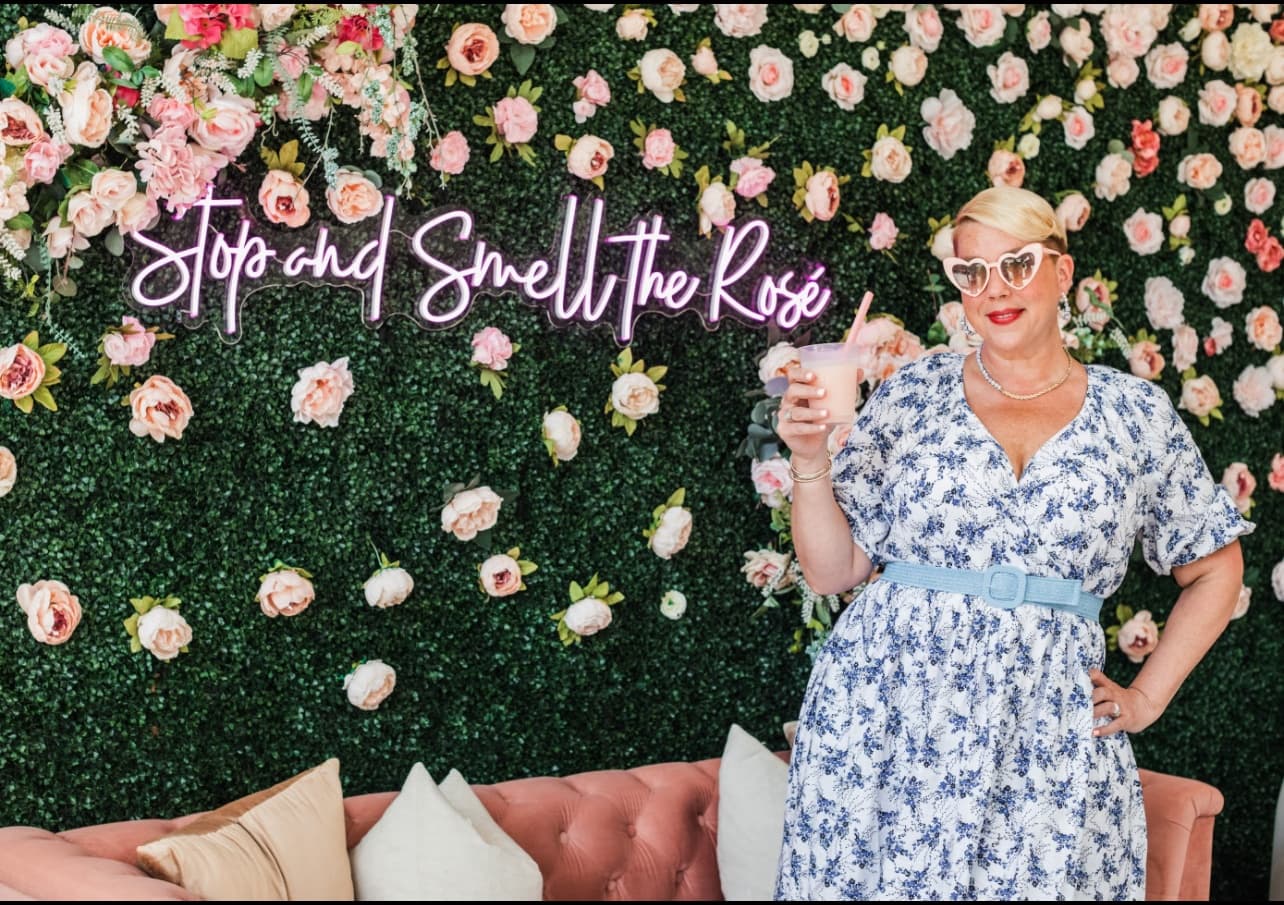 Woman posing with floral wall photo backdrop at event pop-up