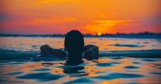 Swimmer floating in calm ocean at colorful sunset