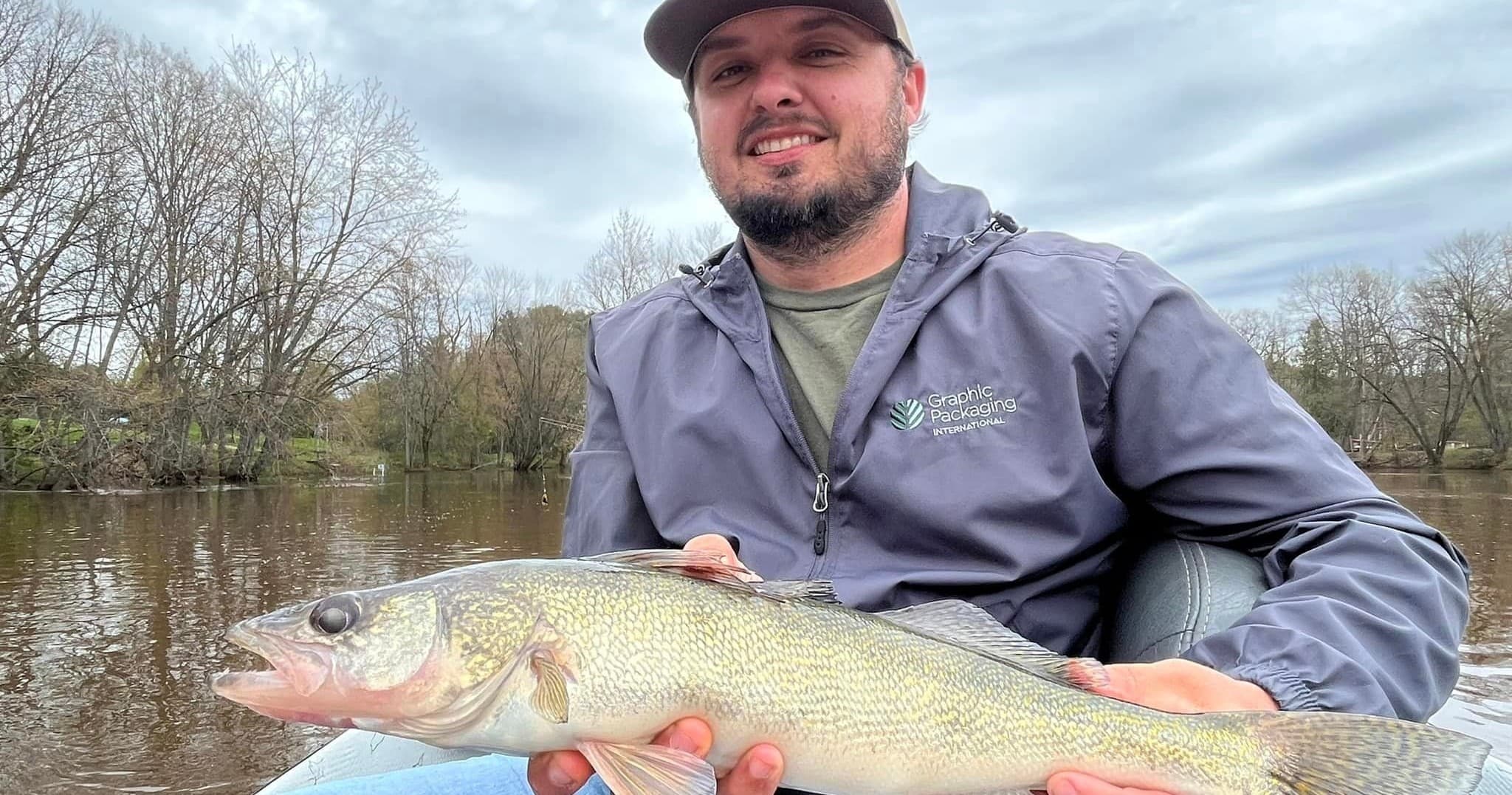Fisherman holding walleye on calm riverbank during day