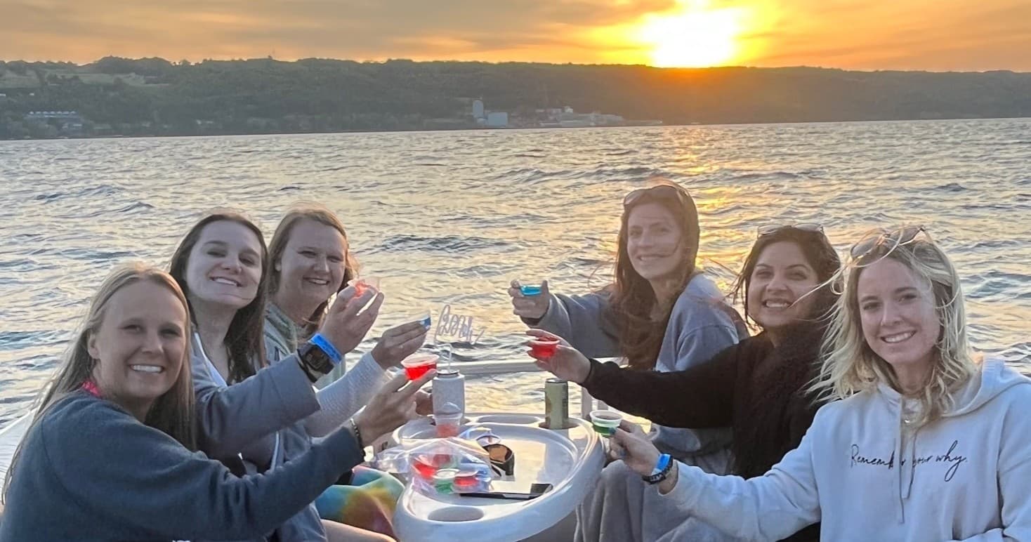Friends raising glasses on pontoon boat at sunset on lake