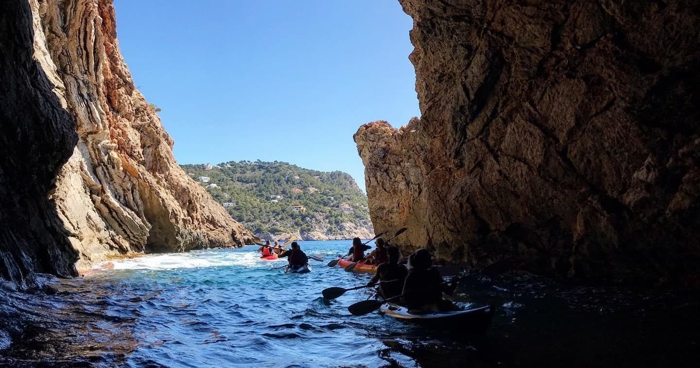 Kayakers paddling through a sea cave toward sunlit coastal vista