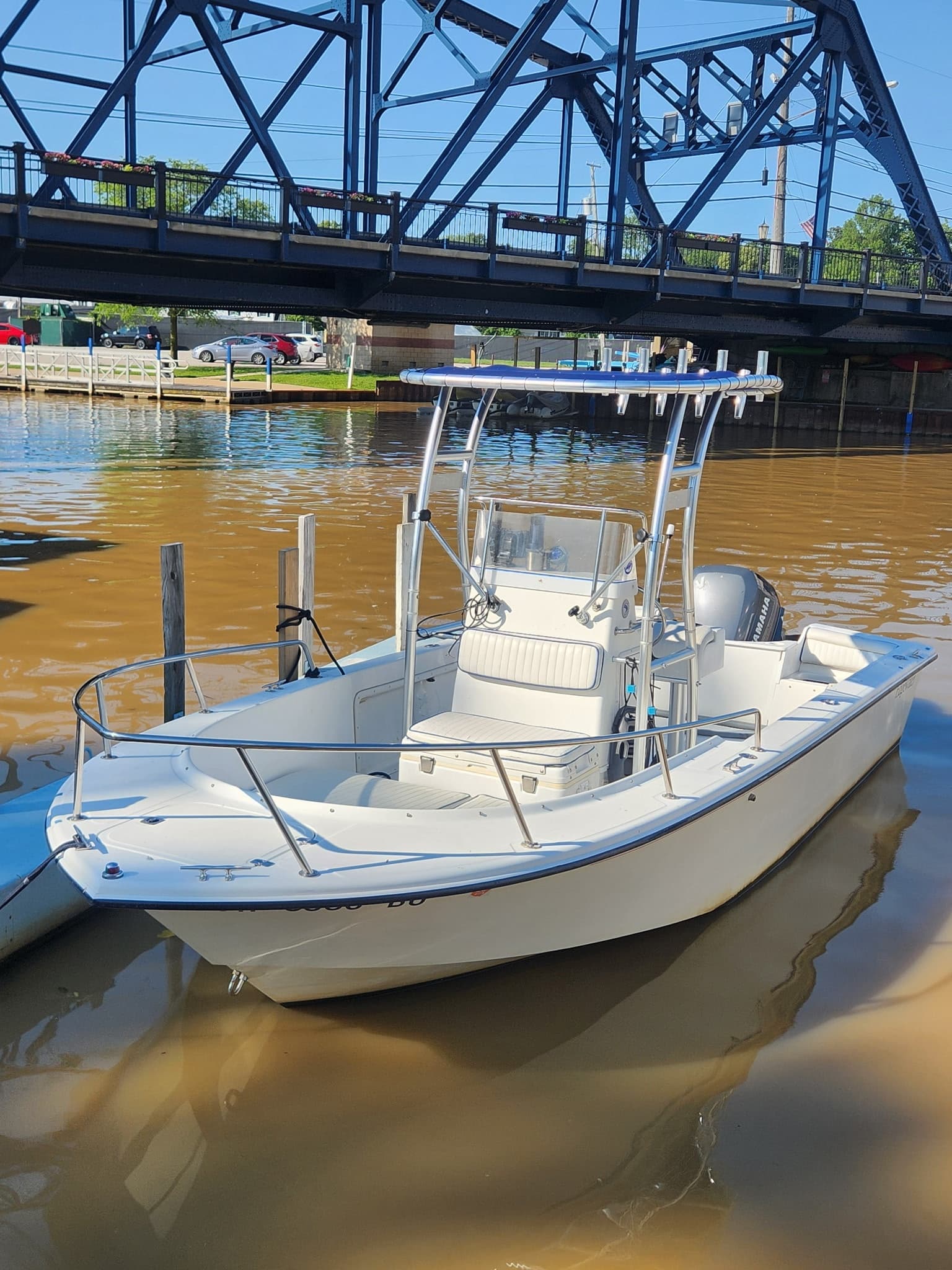 Center-console fishing boat moored under bridge on brown river