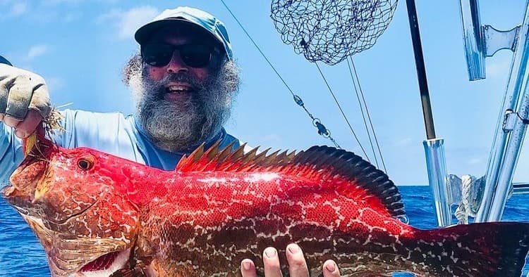 Angler holding large red grouper on sportfishing boat at sea