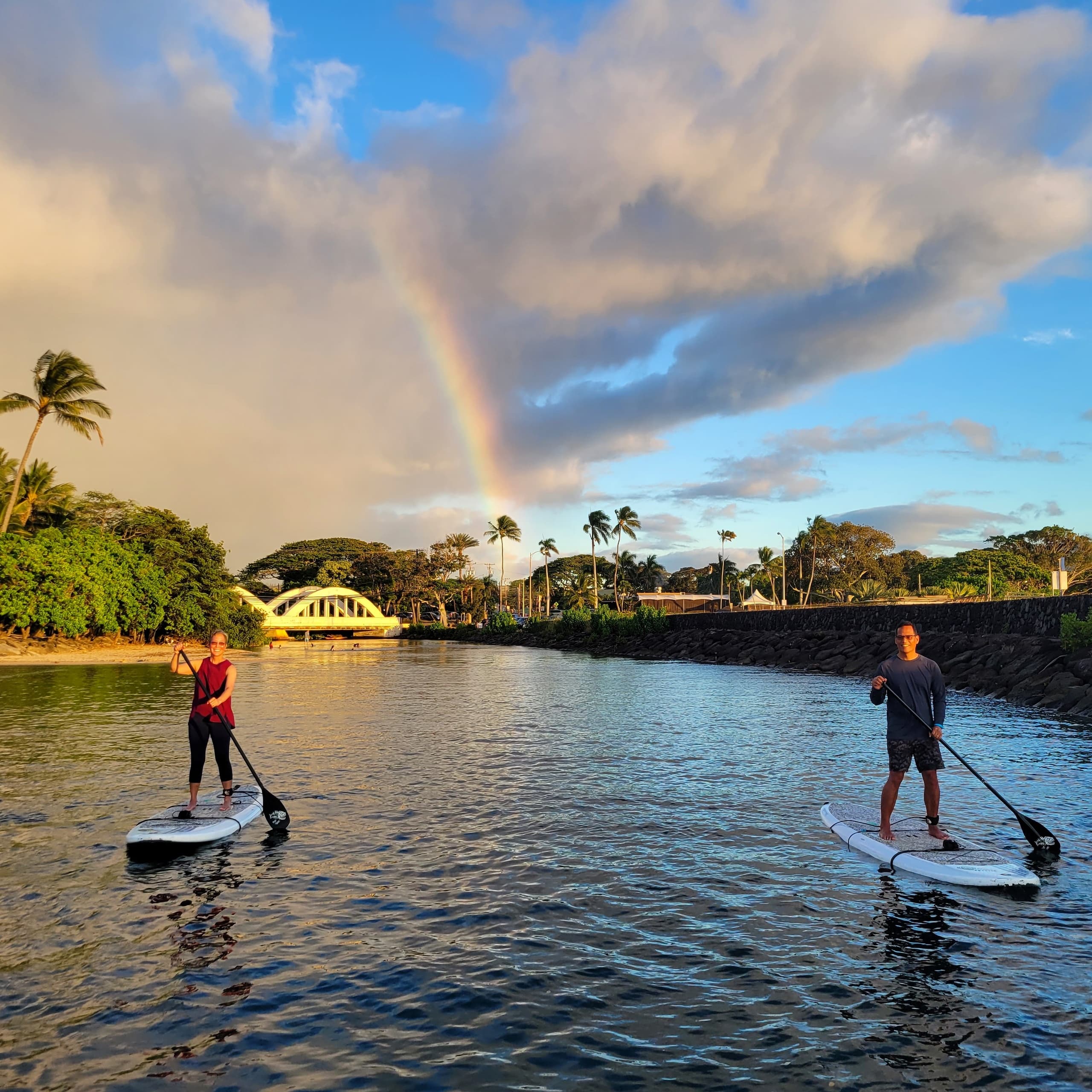 Two paddleboarders at golden hour with rainbow over river