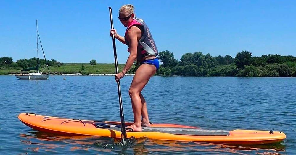Stand-up paddleboarding on calm lake near anchored sailboat