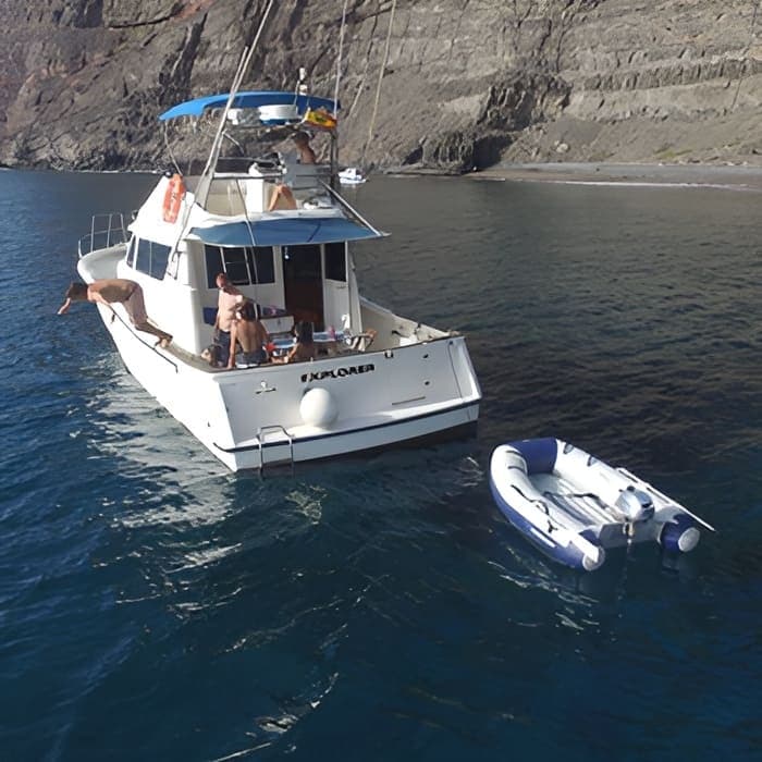 Private motorboat anchored offshore with dinghy and coastal cliffs