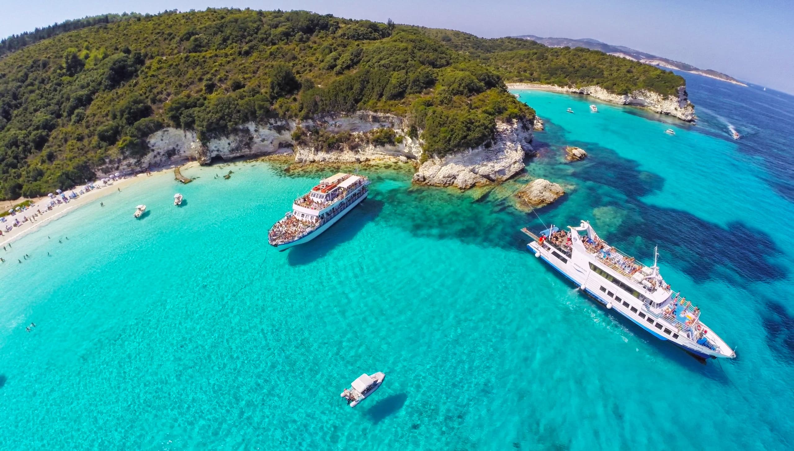 Crystal-blue Ionian beach with anchored excursion yachts
