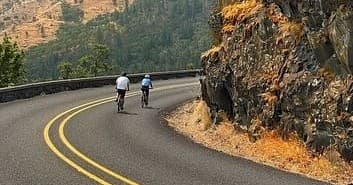 Cyclists riding a scenic winding cliff road through canyon views