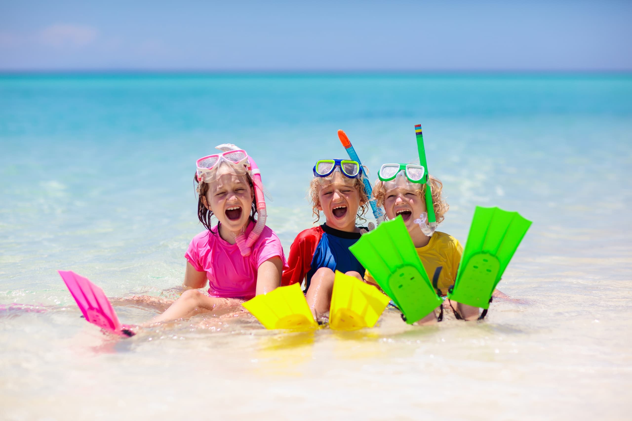 Kids snorkeling and playing with fins on tropical sandy beach