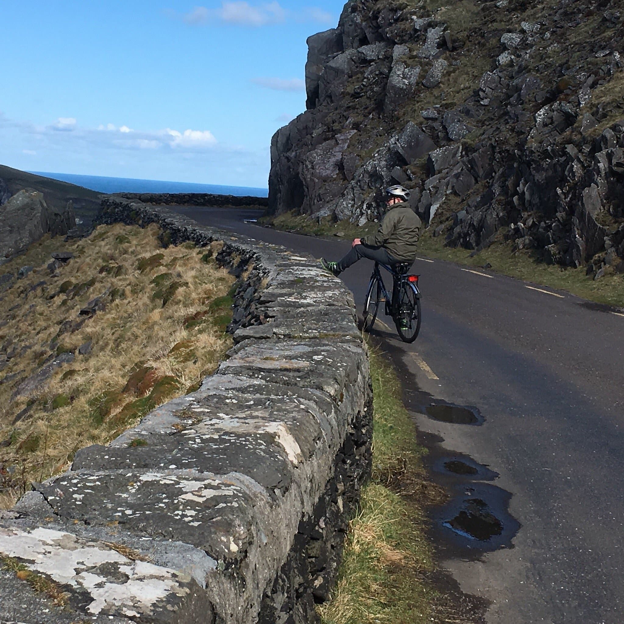 Cyclist pausing on coastal cliff road with ocean views in Killarney