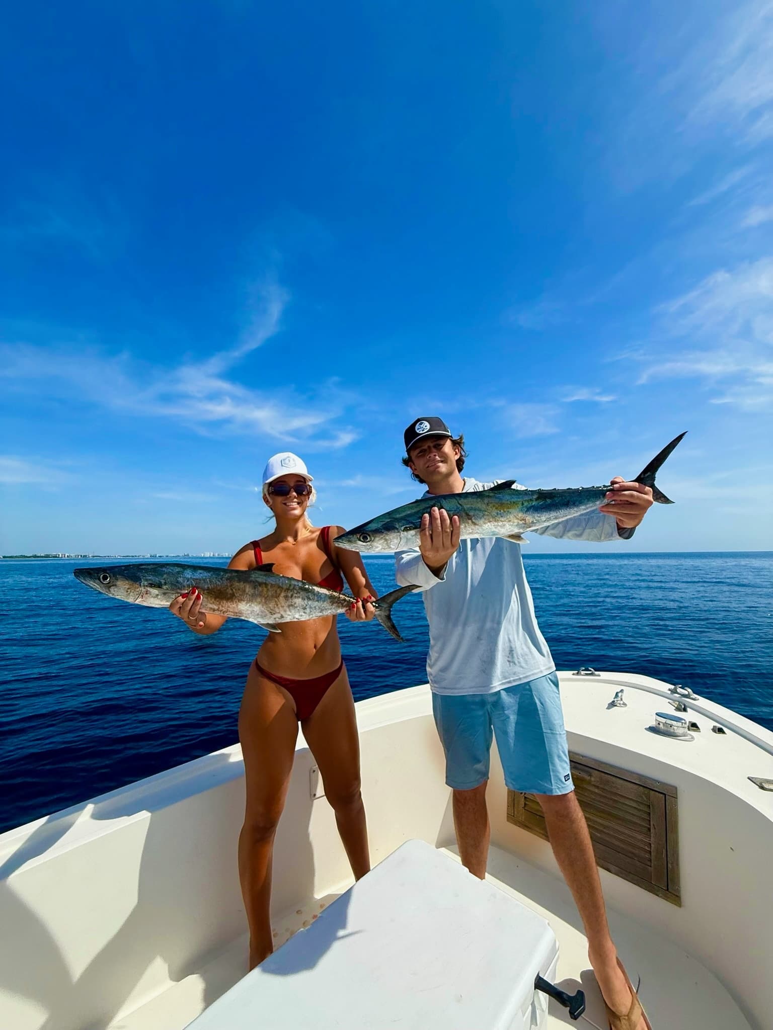 Couple displaying mackerel on bow of boat, blue ocean backdrop