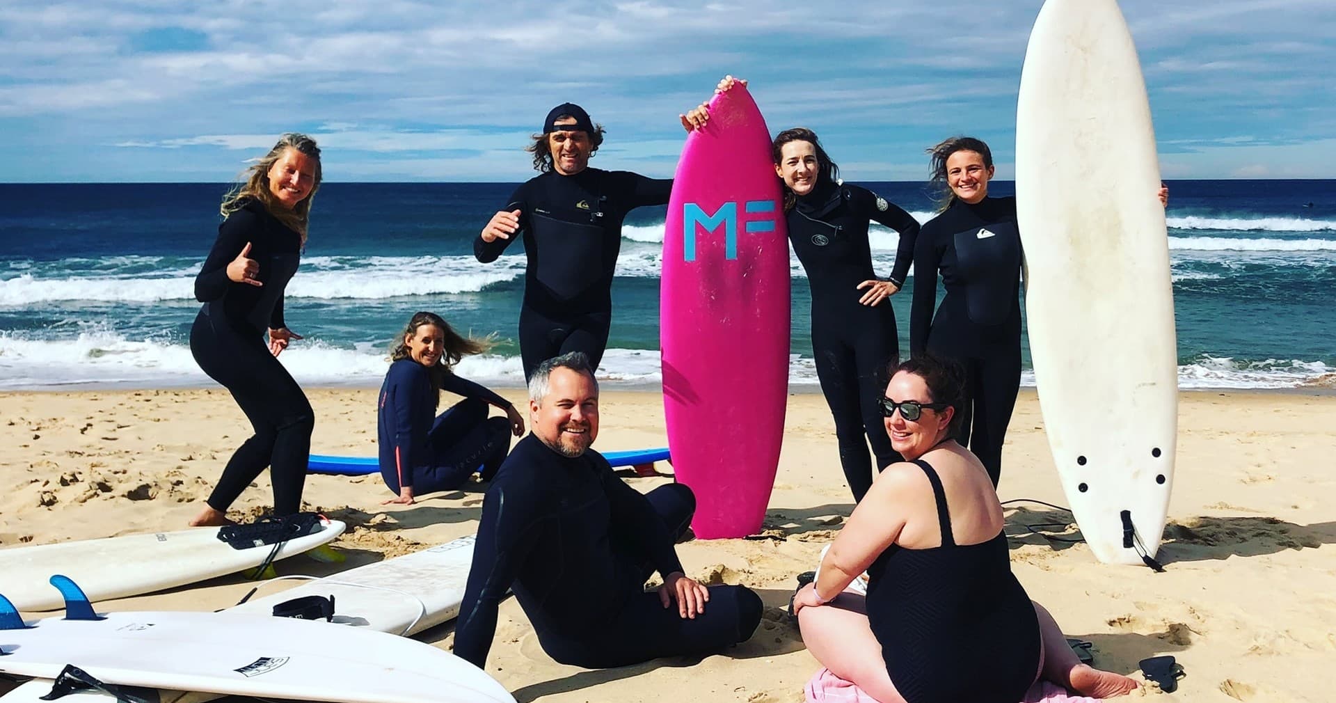 Surf lesson group with colorful boards on sandy beach shore