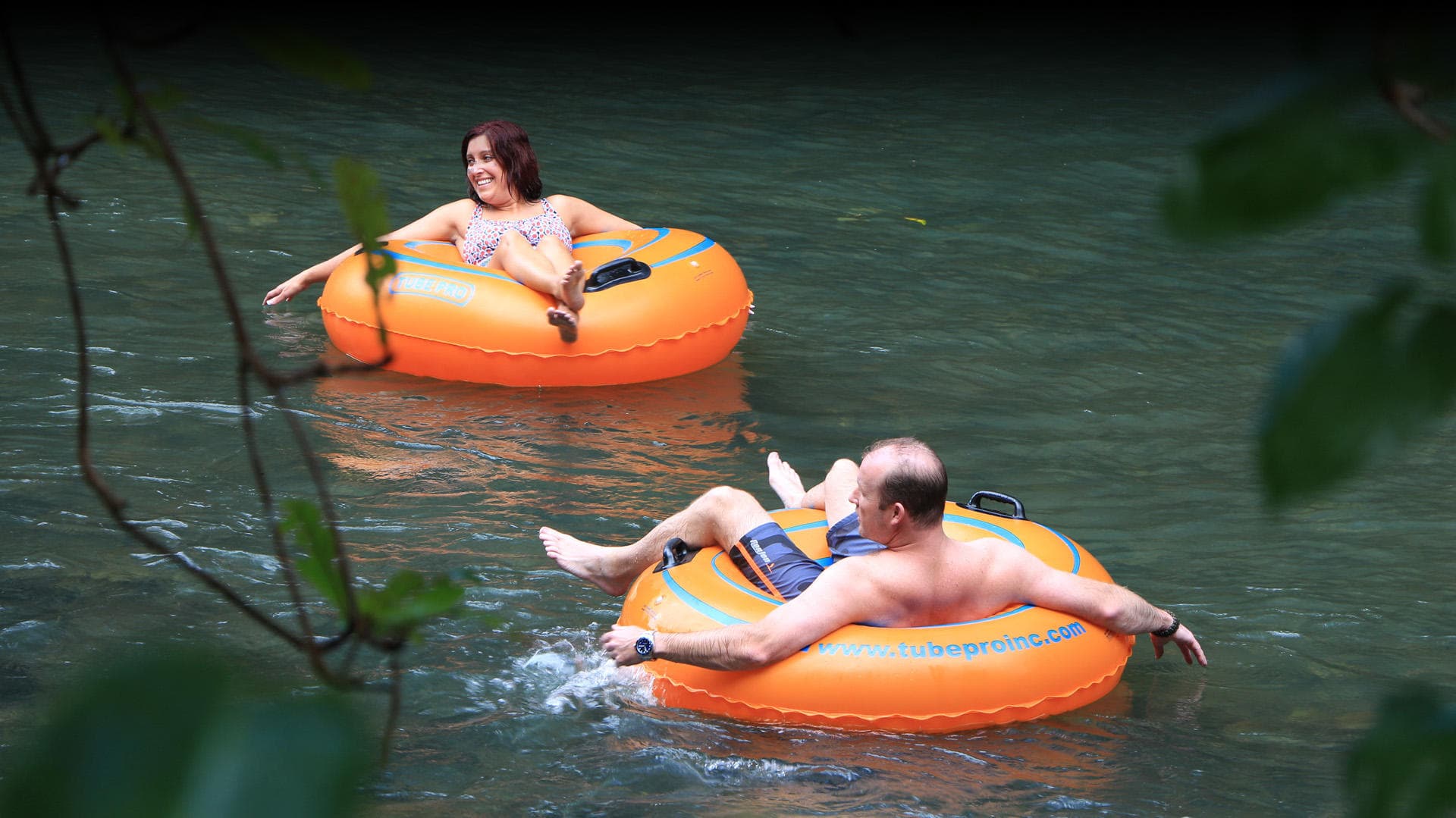 Couple leisurely river tubing in calm jungle river with greenery