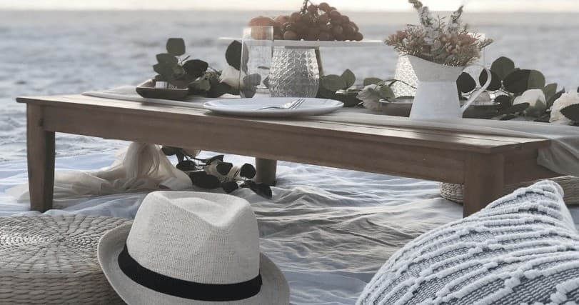 Seaside low picnic table on beach with blanket and hat