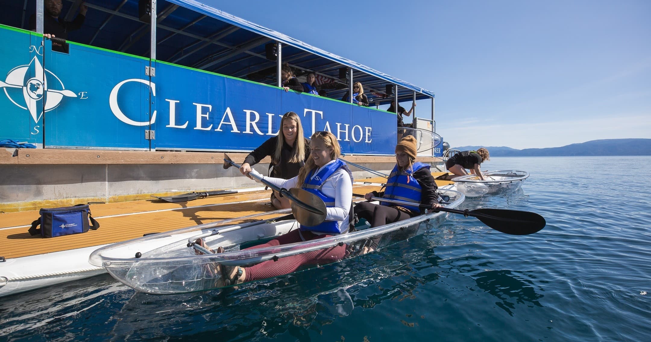 Paddlers launching transparent kayaks from Clear Lake dock on sunny day
