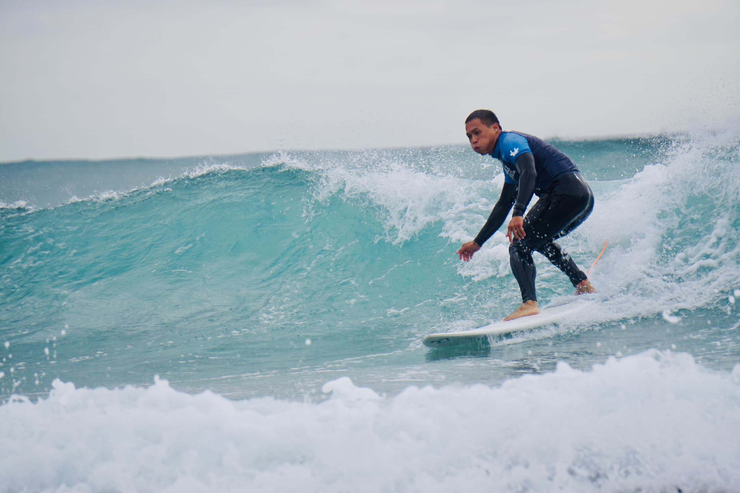 Advanced surfer trimming a turquoise wave off Muriwai Beach
