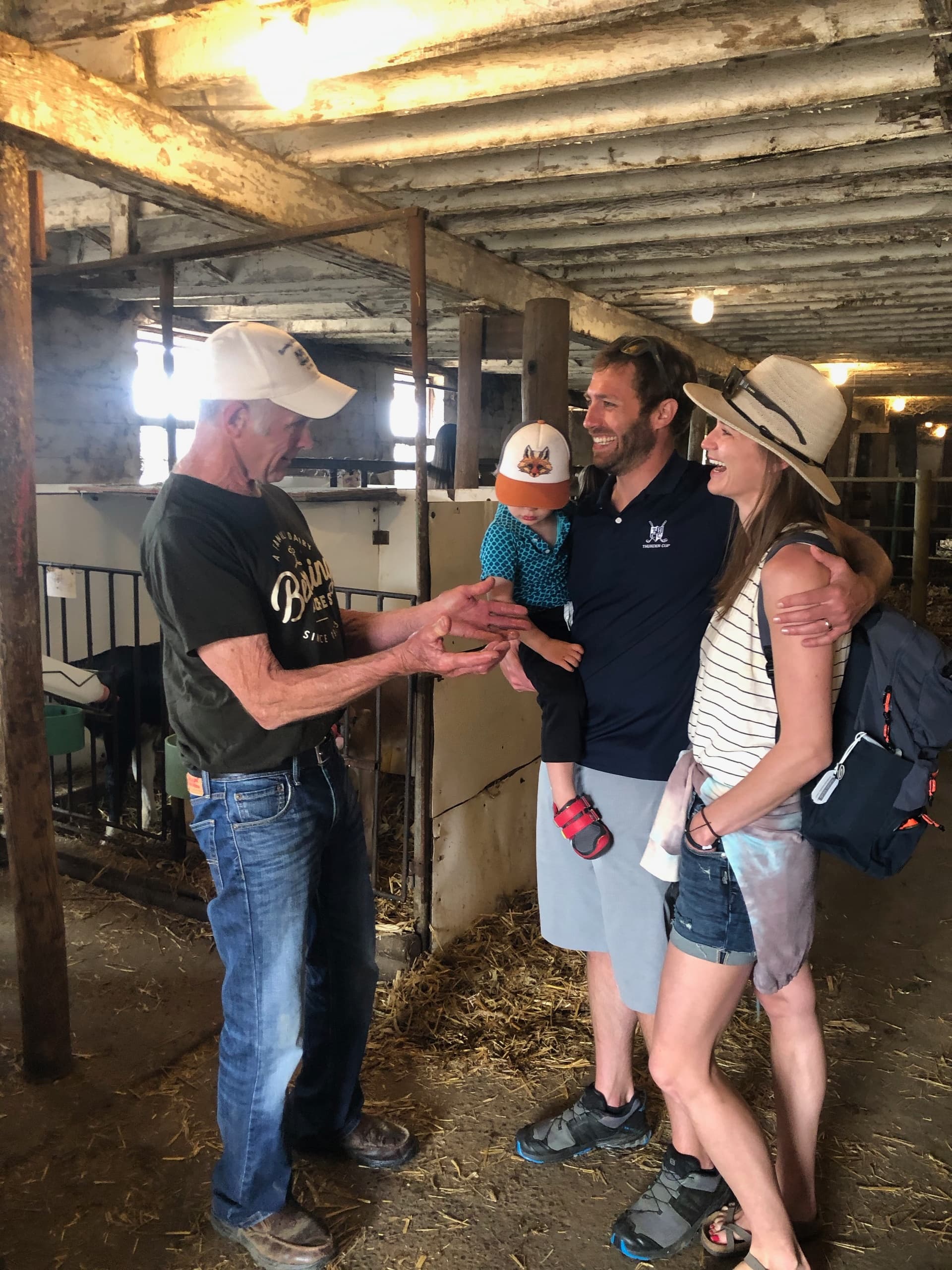 Family conversing with a farmer inside a rustic dairy barn tour