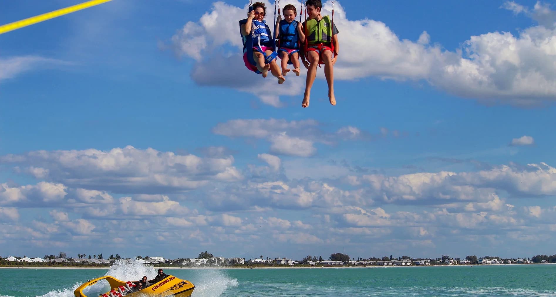 Three people parasailing over turquoise ocean near coastal beach