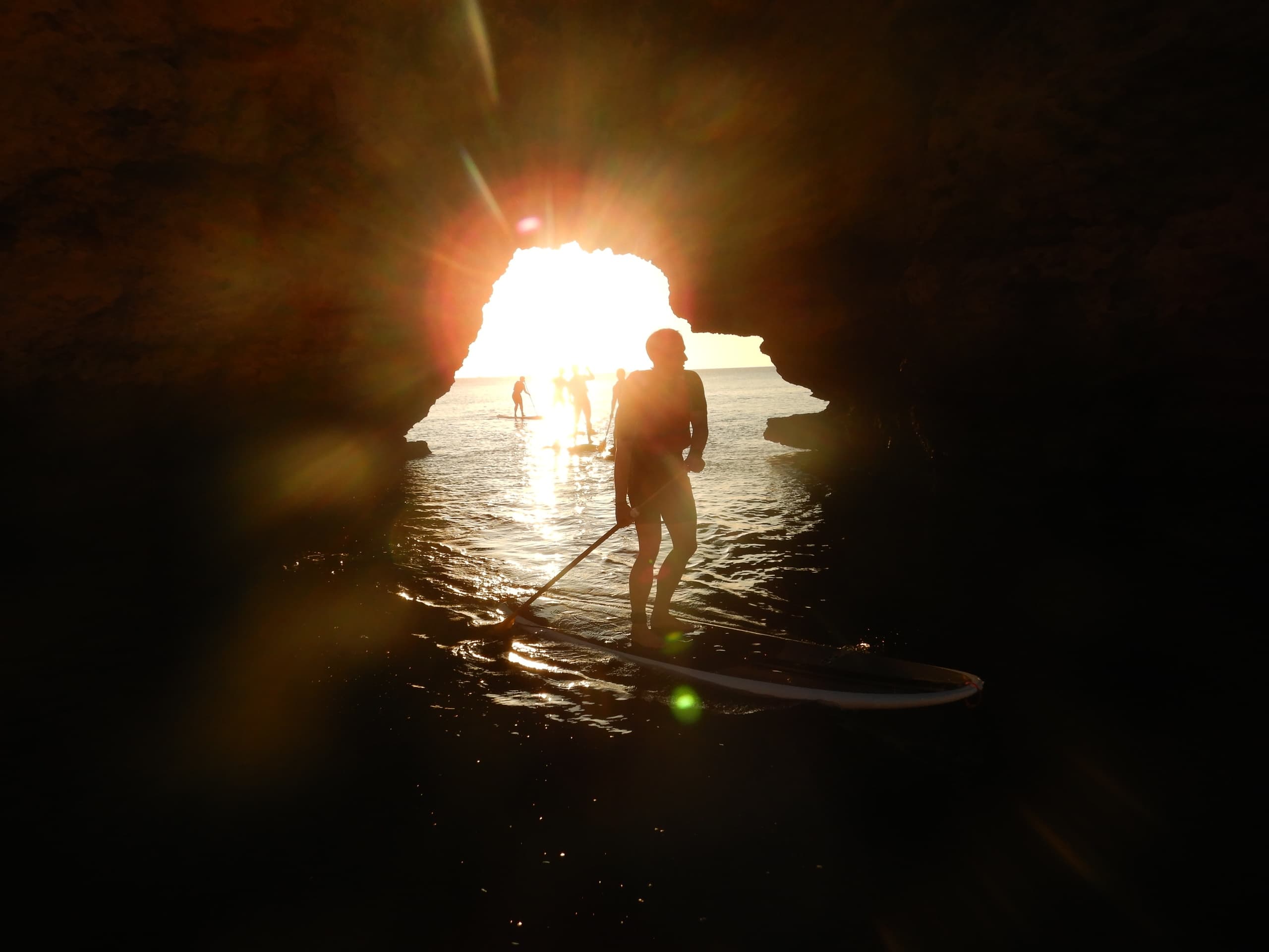 Silhouetted paddleboarder entering sunlit sea cave at Algarve coast