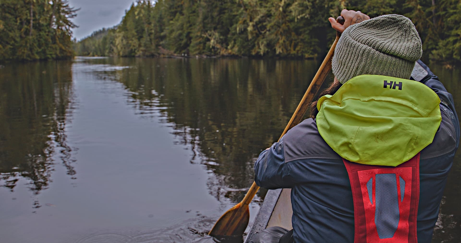 Paddler canoeing through calm inlet, forested shoreline scenery