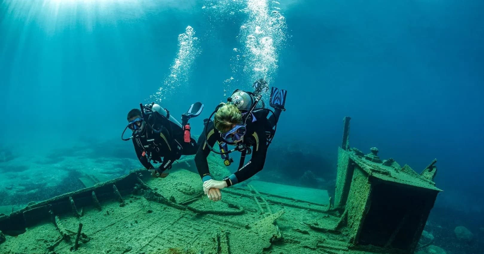 Scuba divers exploring sunken wreck on vibrant coral seafloor
