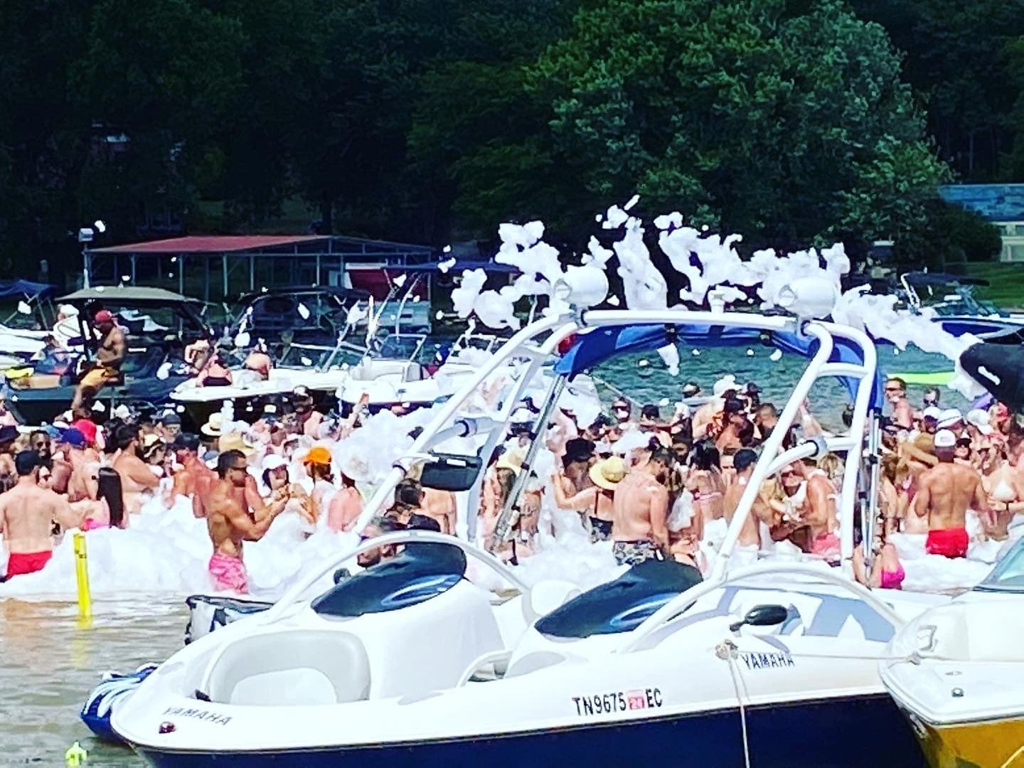 Foam boat party on crowded sunny lake with swimmers and boats