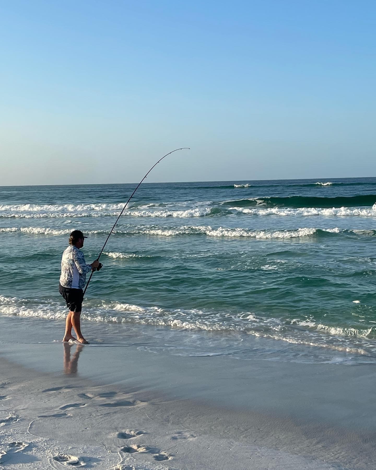 Shore angler surf fishing on sandy beach with rolling waves