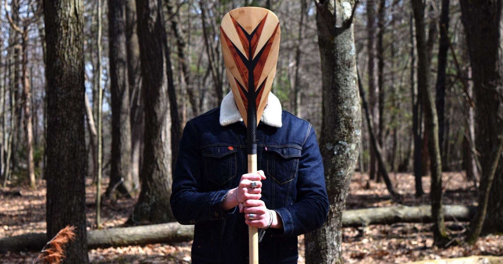 Person holding wooden paddle in wooded forest, paddling gear
