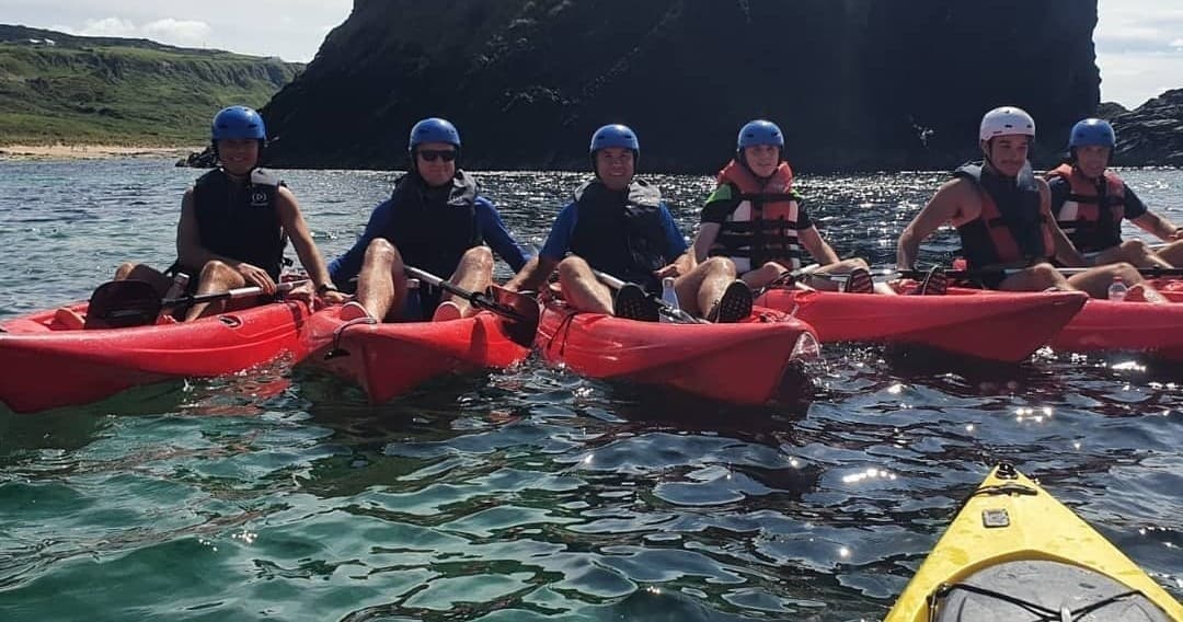 Group of kayakers in red boats near basalt cliffs, guided tour
