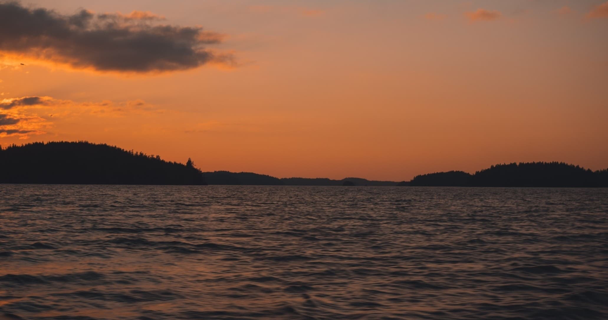 Sunset over calm ocean with silhouetted islands and waves
