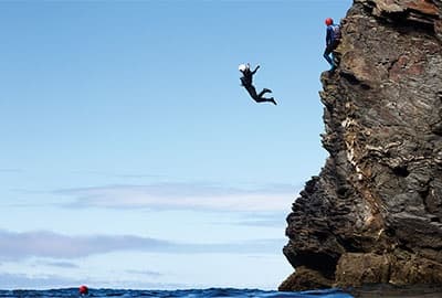 Cliff jumper leaping from coastal rock into open ocean, Cornwall