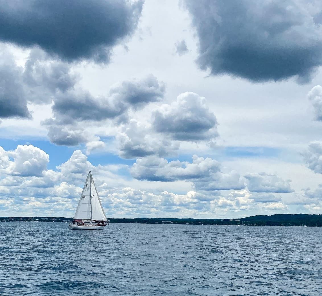 Single sailboat on horizon under dramatic cloudy sky, sailing