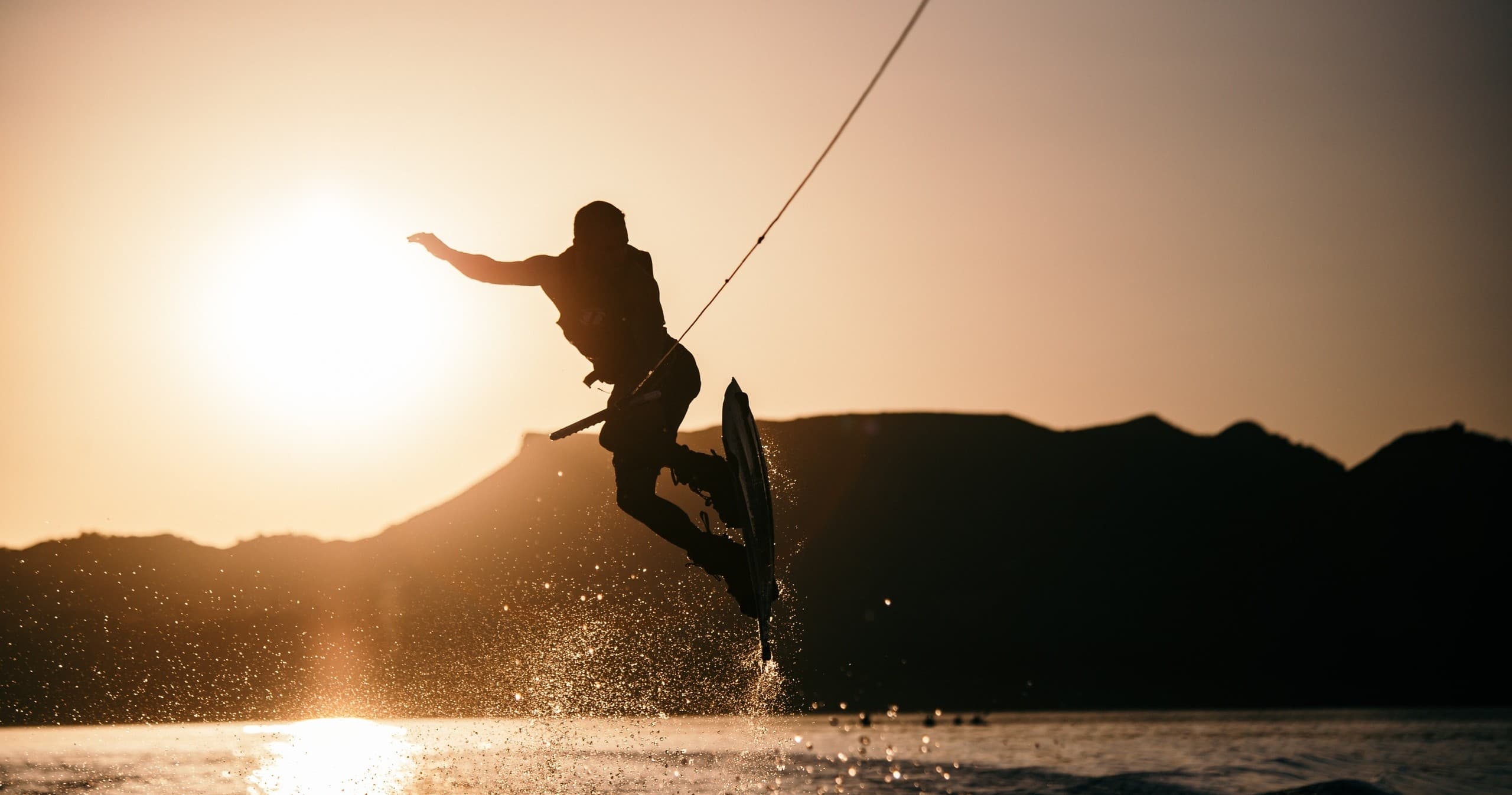 Wakeboarder jumping at sunset over mountain lake, action silhouette